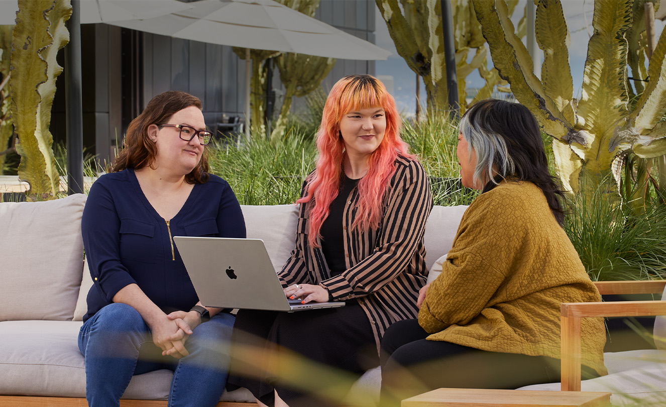 Tre dipendenti Apple sedute all’esterno; una di loro tiene sulle ginocchia un MacBook.