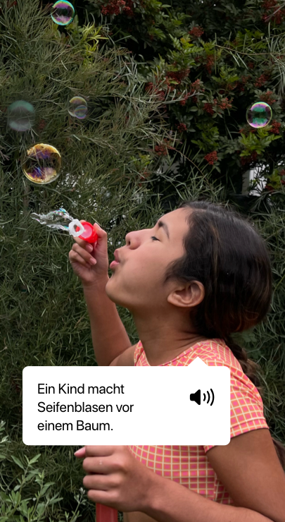 VoiceOver beschreibt ein Foto und zeigt die Sprachausgabe. ‚Ein Kind macht Seifenblasen vor einem Baum.‘