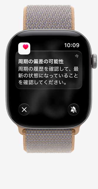 スペースグレイアルミニウムケースのApple Watch Series 12。周期の偏差検知と、ヘルスケアアプリ内の周期記録が表示されている。シャンブレーブルー（ライトブルーグレイ）のスポーツループバンドが取りつけられている