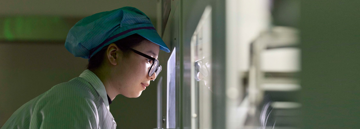 An employee in full-coverage work suit and eye wear observes Apple Watch assembly