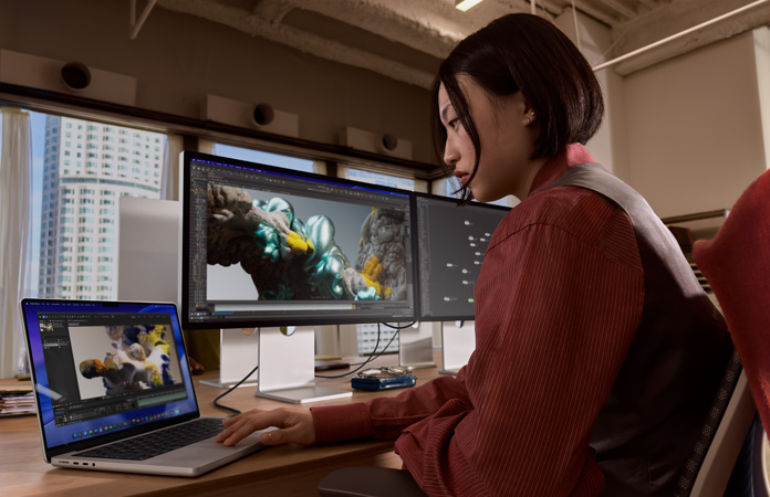 Osoba pracująca w biurze na MacBooku Pro podłączonym do monitora Studio Display XDR