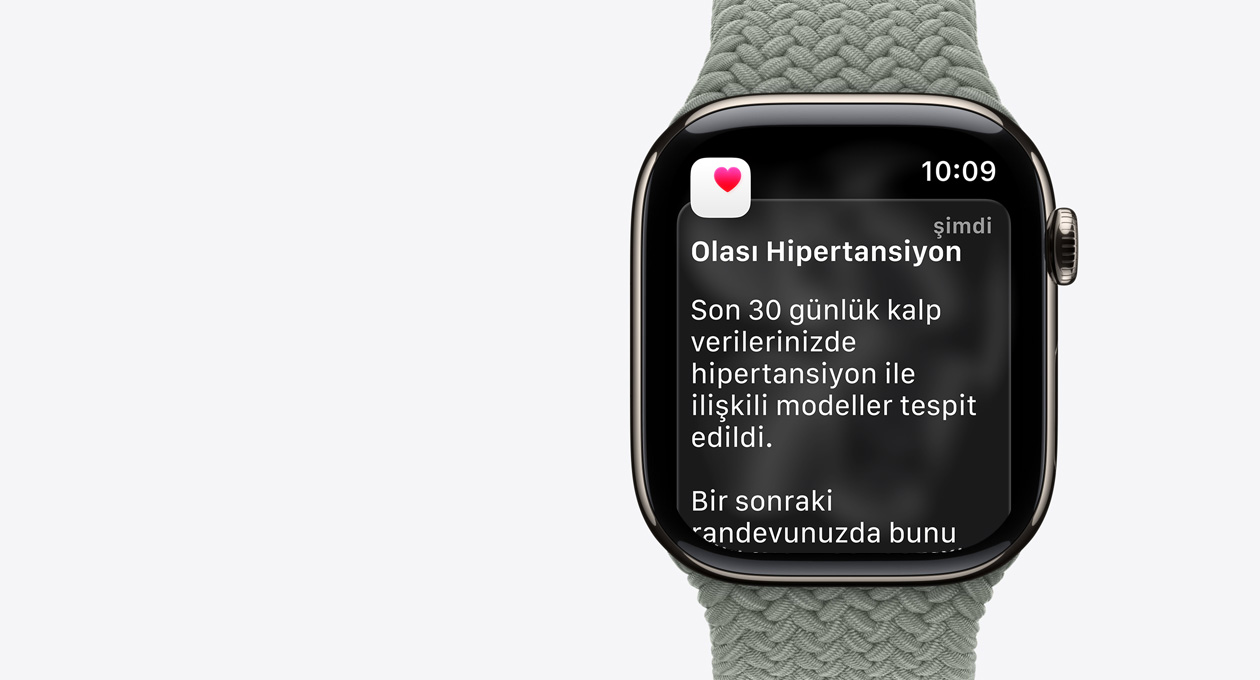Apple Watch Series 11, natürel renk, titanyum kasa, olası hipertansiyon bildirimi, beyaz kutu içinde pembe kalp, sağ dış görünüm, Digital Crown, kordon, yeşil gri renkte Örgü Solo Loop