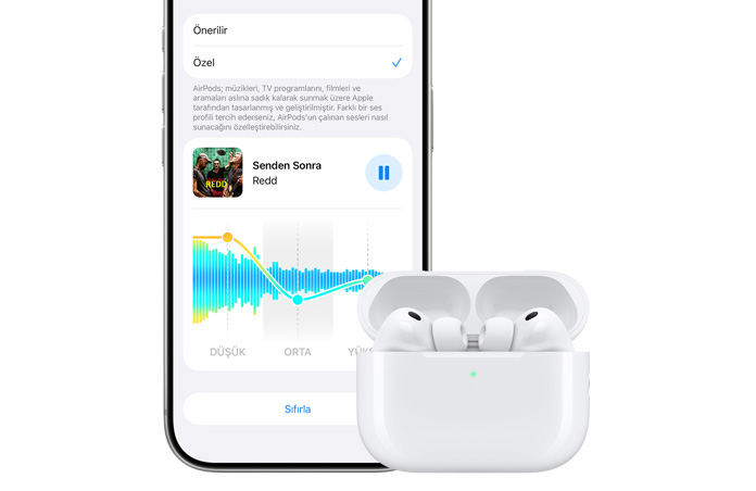 iPhone 18 Pro, önden görünüm, beyaz şarj kutusunun içindeki kulaklıklarla birlikte açık duran Apple AirPods Pro 3’ün yanında duruyor
