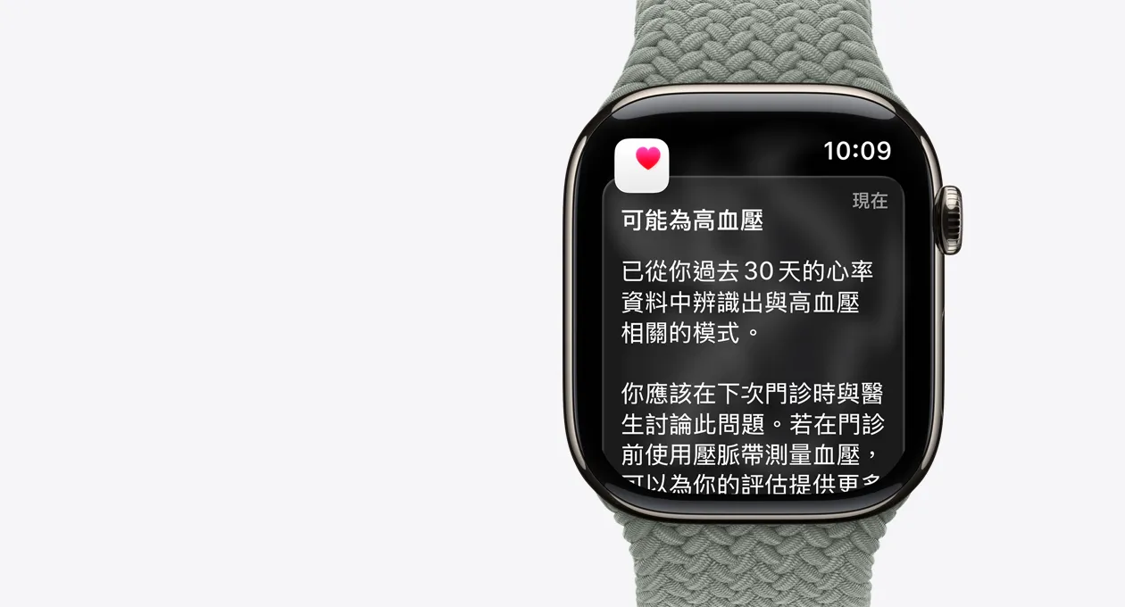 Apple Watch Series 11，展示原色鈦金屬錶殼，搭配綠灰色單圈錶環，螢幕顯示可能為高血壓的通知，圖示為白色方框內的粉色愛心，機身右側展示數位錶冠