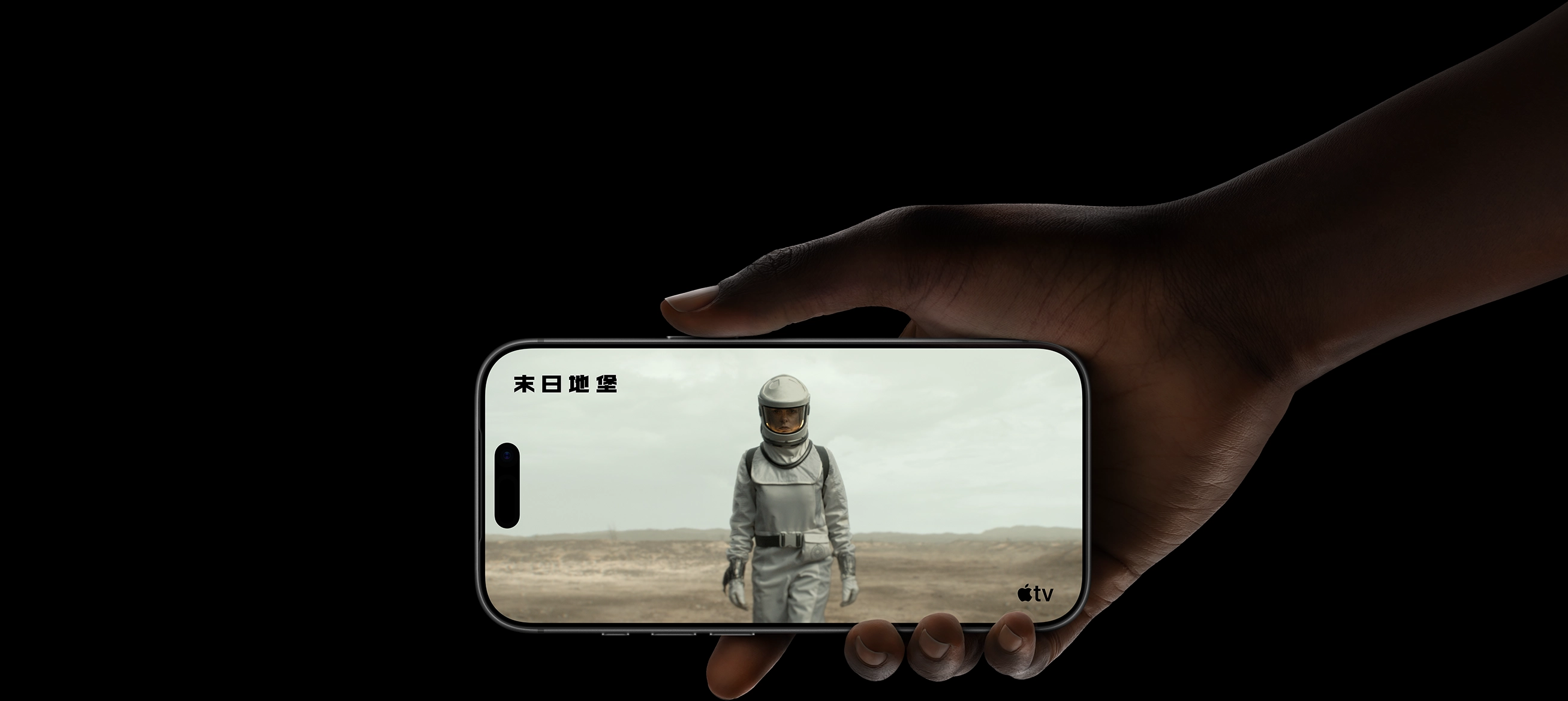 一隻手拿著 iPhone 17 Pro，螢幕顯示一名身穿防護服並戴著頭盔的女子，行走於荒涼的景色之中。Apple TV 標誌，影集片名：末日地堡