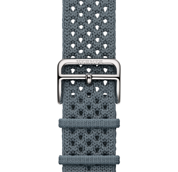 Apple Watch Hermès Series 11 con correa Néo Tricot, color Bleu Gris (gris azulado), fabricada con hilo de poliamida tejido, orificios de ajuste en el centro, hebilla color plata con “Hermès” grabado
