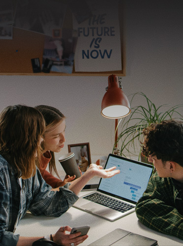 Three students collaborate around an open MacBook Pro, showing how familiar devices make it easy to transition into the workforce
