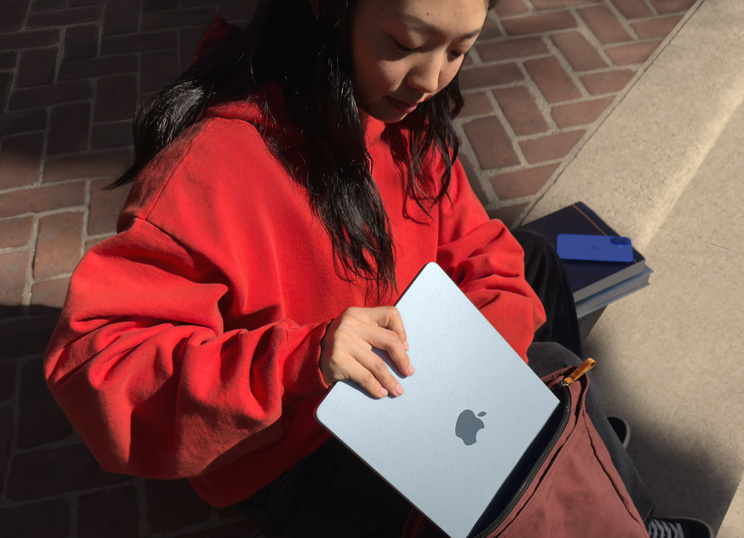 Kivirappusilla istuva henkilö panee MacBookia reppuun.