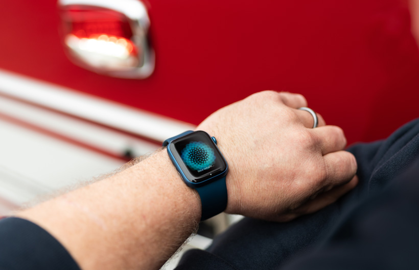 En arm med et Apple Watch viser en besked med teksten: Now inhale, og en brandbil står i nærheden