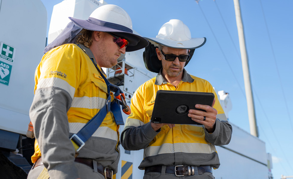 Deux agents de terrain travaillent ensemble sur un iPad, à côté d’un camion utilitaire