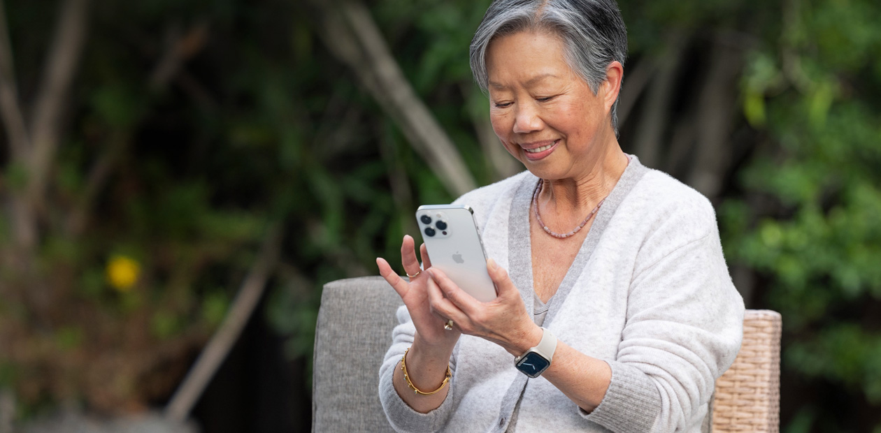 Une femme âgée assise sur une chaise consulte un iPhone.
