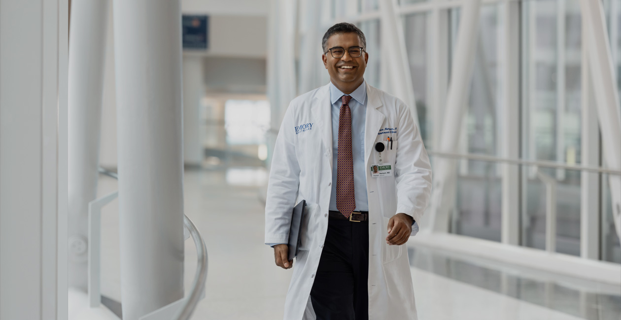 Un médico camina con un MacBook bajo el brazo derecho.