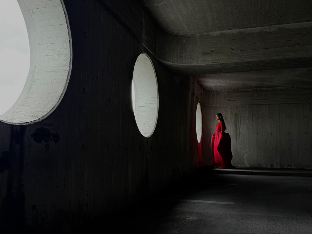 Una donna con un lungo vestito rosso fotografata in piedi in una stanza vuota. Nell’app Foto la lunghezza focale viene regolata a 35 mm, per mettere in evidenza le capacità del sistema di fotocamere Pro