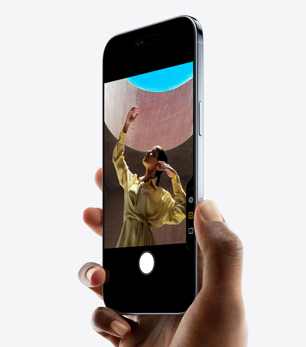 Kézben tartott iPhone Air ferdén elölnézetből, a kéz hüvelykujja a Kameravezérlő gombon van. A kép bemutatja a készülék vékony profilját, a Dynamic Islandet és az oldalsó gombot.