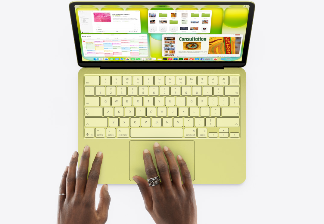 MacBook Neo, citrus color, a person's hand on trackpad, multiple windows open including Music, Calendar, and Microsoft PowerPoint apps