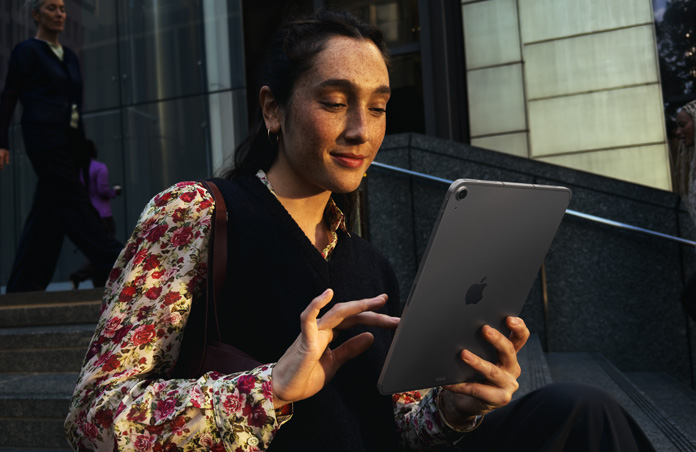Person sitting on steps outside a large building using an iPad Air 11 in Space Grey, maintaining seamless Wi-Fi connection across network transfers